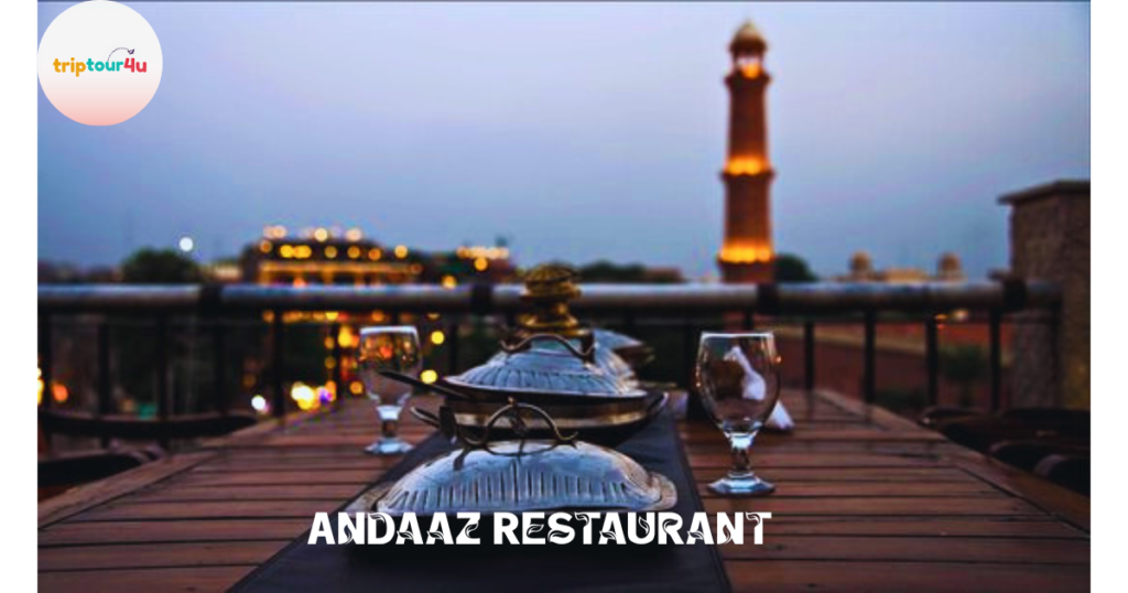Rooftop dining setup at Andaaz Restaurant with traditional serving dishes and glassware, overlooking illuminated historic minaret and city lights at dusk in Lahore, Pakistan.