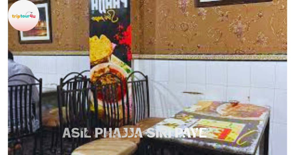 A sideways photo of a restaurant interior showing a wooden table set with plates of food, black metal chairs, and a person in colorful traditional clothing standing near the table. 
