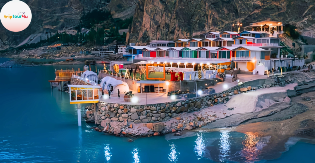 Evening view of Luxus Hunza Resort built on the lakeside, featuring colorful hillside villas, illuminated walkways, and turquoise water reflecting the lights.