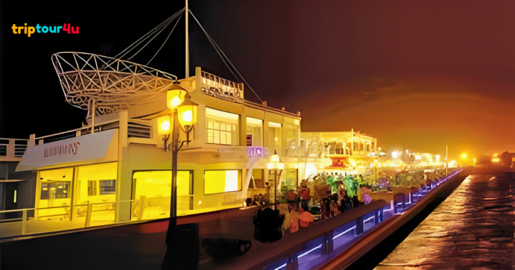 Port Grand Karachi at night, featuring illuminated restaurants and cafes along the waterfront promenade, with vibrant lights reflecting on the sea.