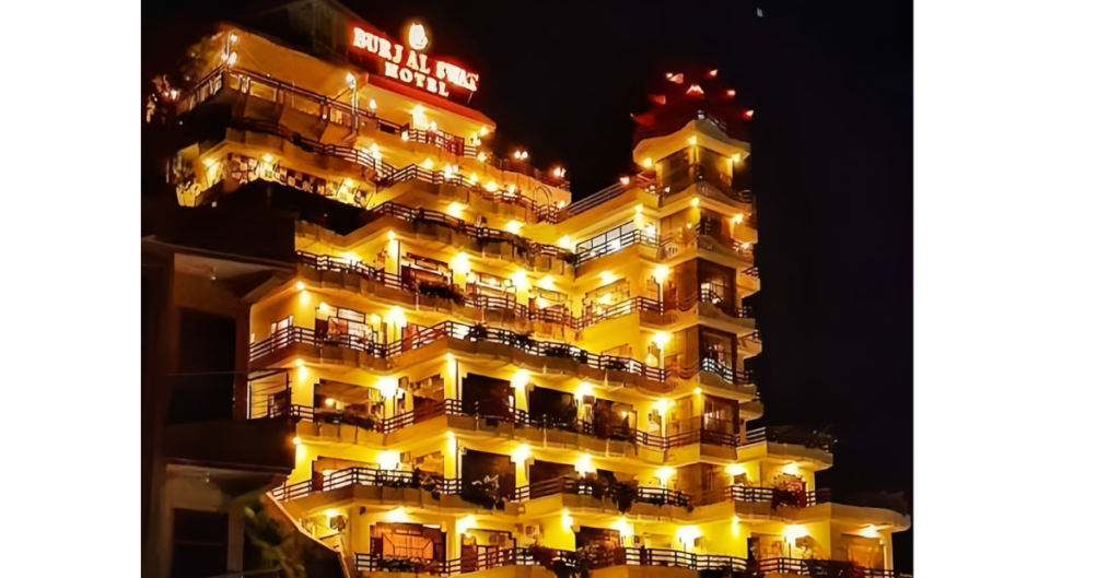 Night view of Burj Al Swat Hotel featuring a tall, multi-story building illuminated with bright golden lights and layered balconies creating a striking architectural look.
