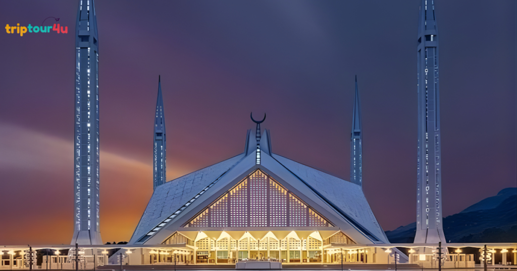 ​A striking nighttime view of the Faisal Mosque in Islamabad, featuring its iconic tent-like triangular structure illuminated with warm yellow lights. Four tall, slender minarets frame the central building against a deep purple and orange twilight sky.