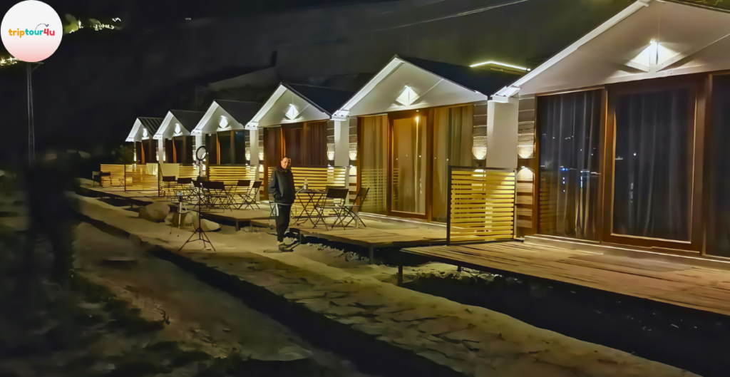 Night view of Horizon Resort Hunza featuring modern wooden cabins with warm lighting, private outdoor seating areas, and a guest walking along the illuminated pathway.