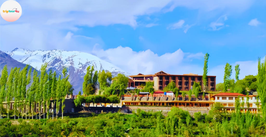 Exterior view of Serena Hunza Baltit Inn surrounded by green trees, with snow-covered mountains and a bright blue sky in the background.