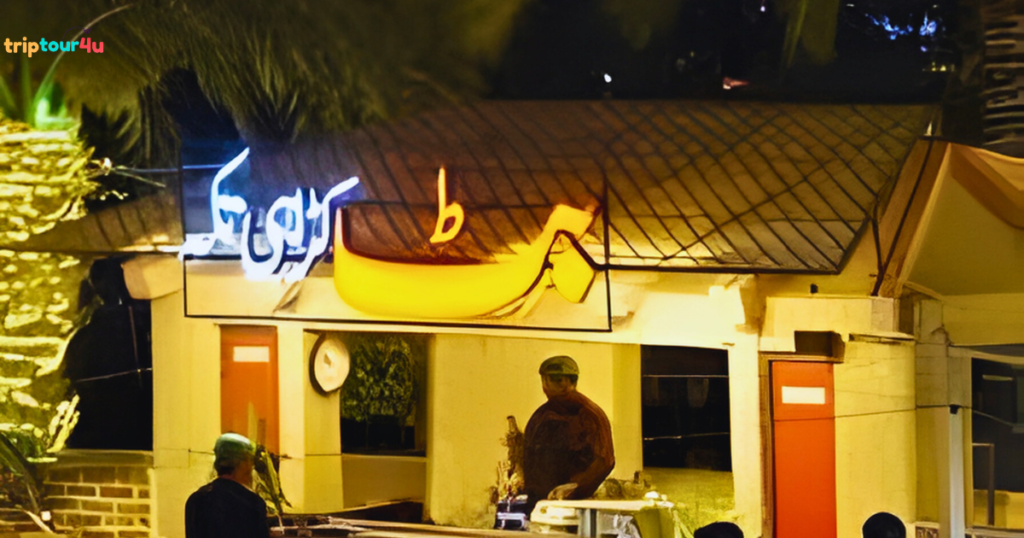 Night view of Butt Karahi restaurant with illuminated Urdu signage and chefs preparing food at the outdoor cooking area.