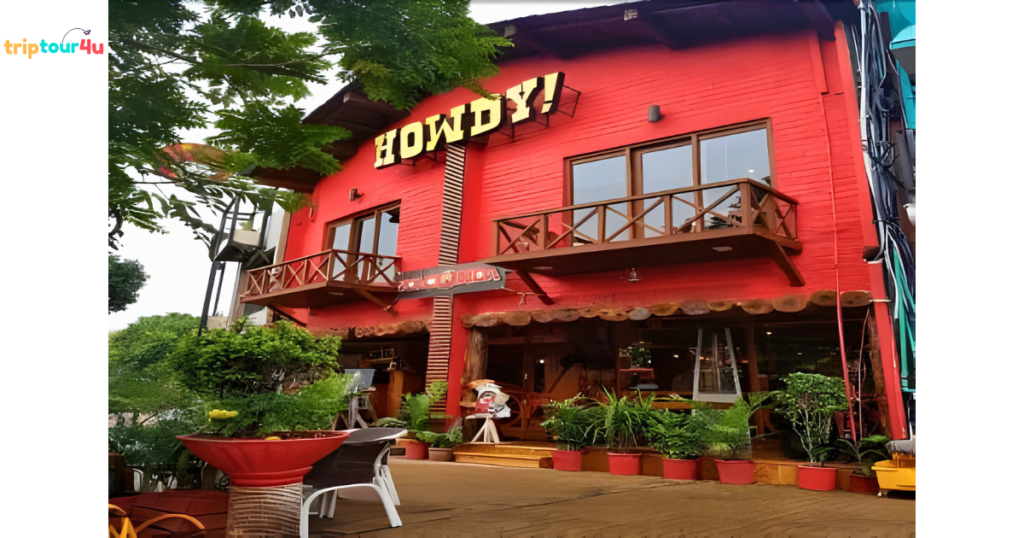 Exterior of Howdy restaurant featuring a bright red two-story building with wooden balconies, large windows, greenery in potted plants, and a welcoming entrance surrounded by trees.