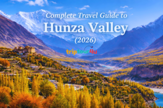 Scenic Hunza Valley view with autumn foliage, Baltit Fort, Karimabad village, and snow-capped Karakoram peaks under a clear blue sky.