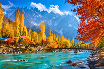 Autumn landscape in Northern Pakistan with golden trees, turquoise river, and snow-capped mountains under a clear blue sky.