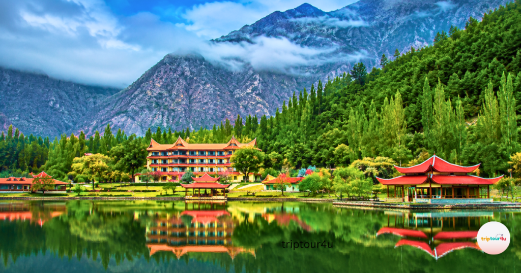 Skardu after summer travel at Shangrila Resort on Lower Kachura Lake, featuring calm crystal-clear water, red-roof cottages, lush green trees, and majestic Karakoram mountains reflected under a blue sky.