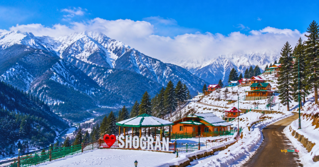 Snow-covered Shogran in Kaghan Valley with wooden cottages, pine forests, winding mountain road, and scenic Himalayan peaks on a clear winter day.